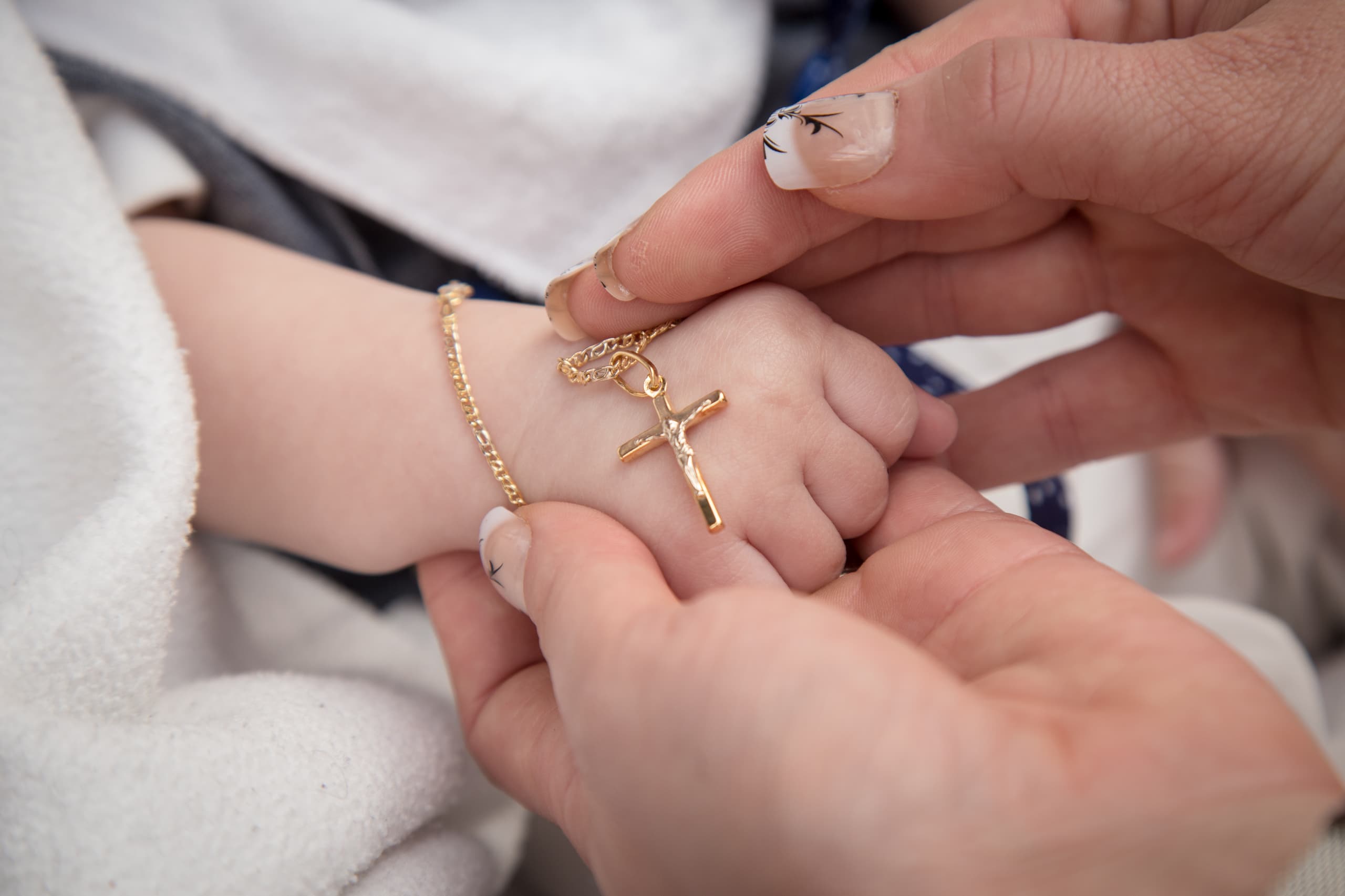 Gold cross necklace in baby's hand for baptism